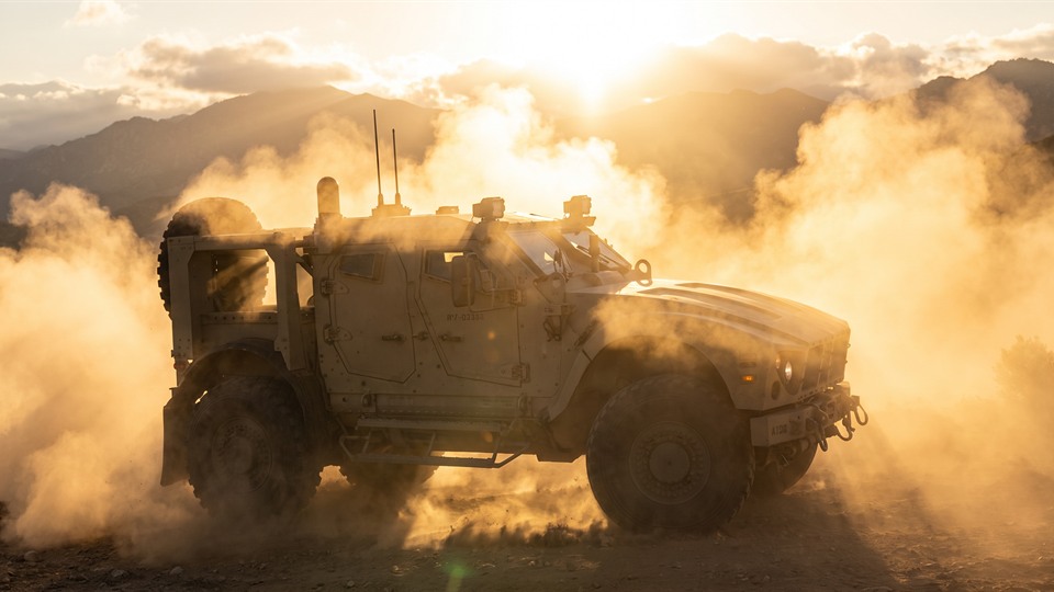 A tactical vehicle crossing a dusty mountain landscape at sunset.